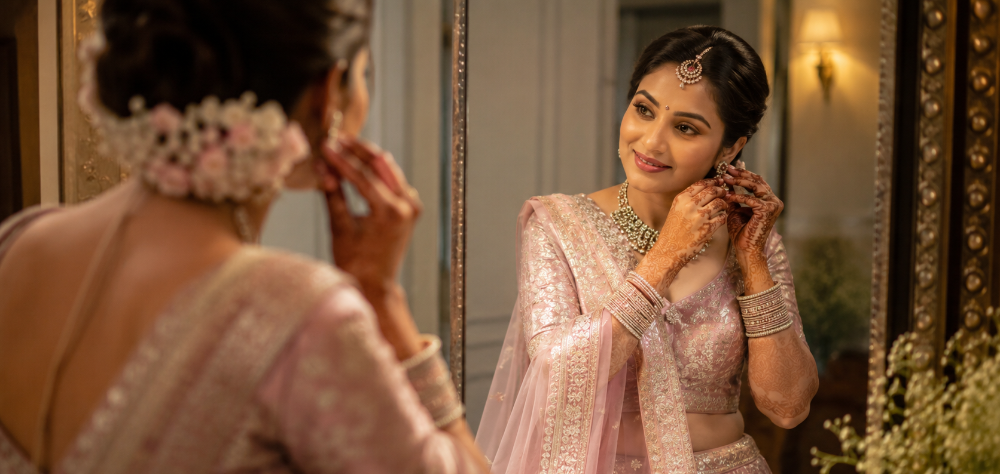  Bride adjusting her jewelry while wearing a stunning pastel pink Banarasi silk lehenga