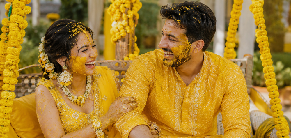 Bride and groom laughing on a swing with turmeric paste on their faces
